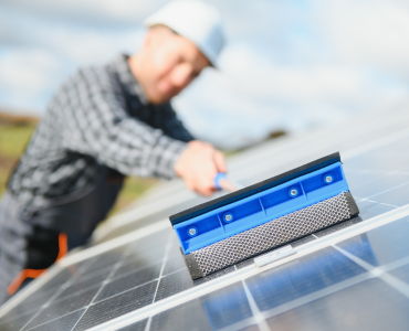 Man using cleaning tool on solar panels with blue sky.